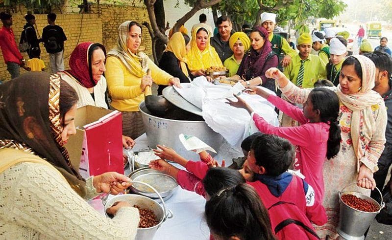 ਬੱਚਿਆਂ ਅਤੇ ਭਾਈਚਾਰਕ ਮੈਂਬਰਾਂ ਨੂੰ ਬਾਹਰ ਭੋਜਨ ਵੰਡਦੇ ਸਵੈਸੇਵਕ।
